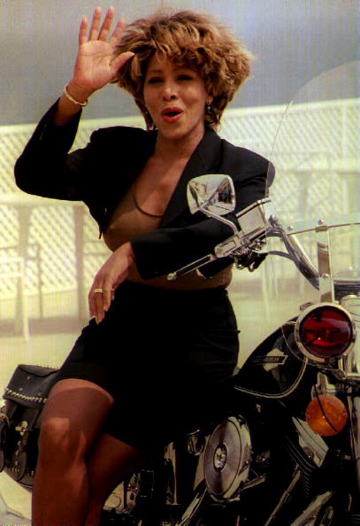 Tina Turner perched on a motorcycle poses for the
